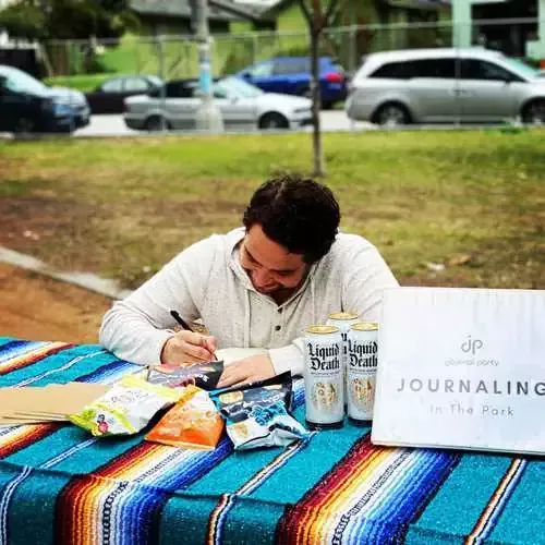 Person writing by hand in a paper journal outside