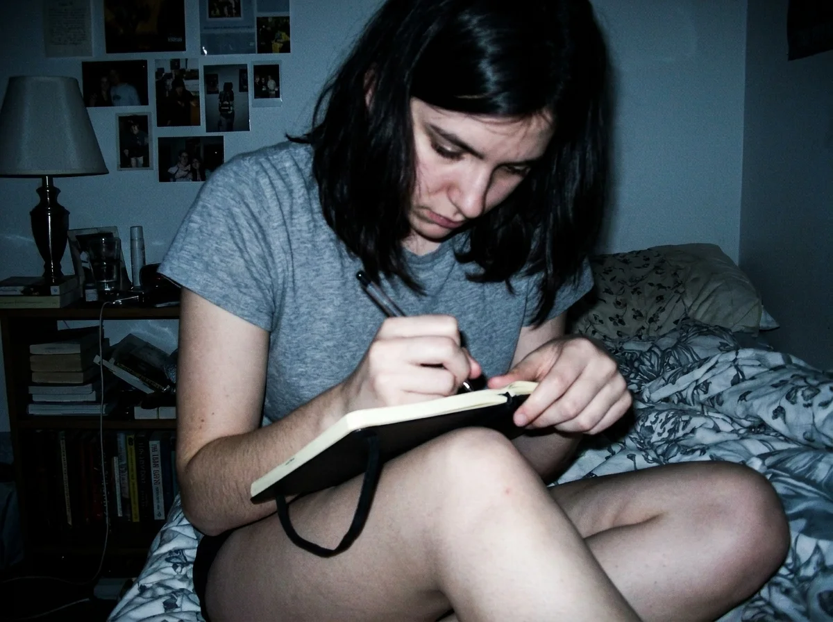 Person writing by hand in a paper journal on a bed