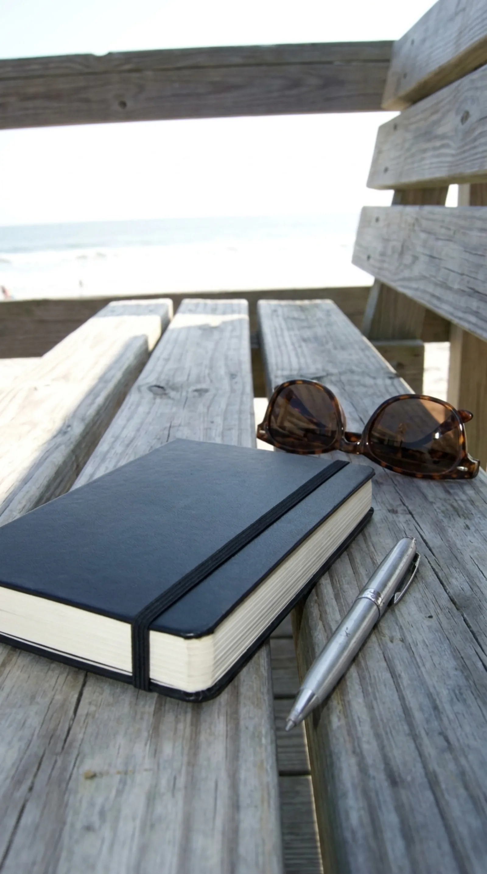 Open paper journal and pen on a sunny beach boardwalk