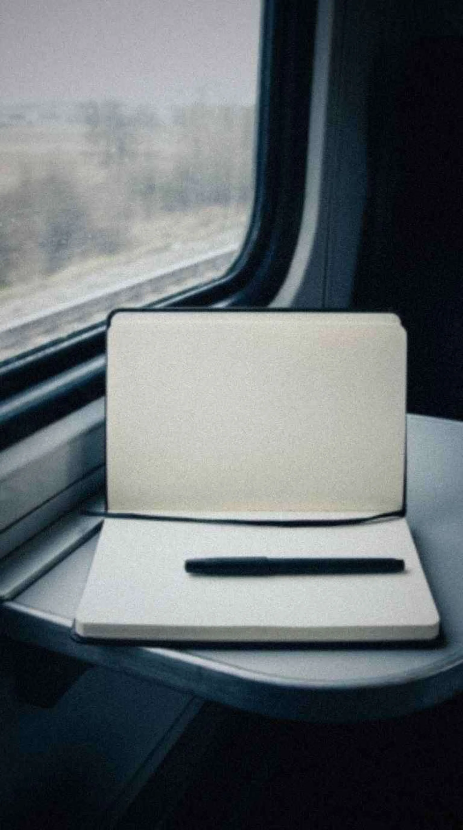 Open paper journal on a train table beside a window with passing scenery